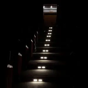 A dark cinema room with maintained emergency lighting illuminating the stairway