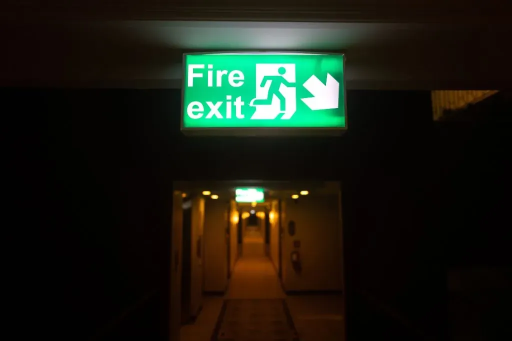 A fire exit down right sign lit up in a dark hallway