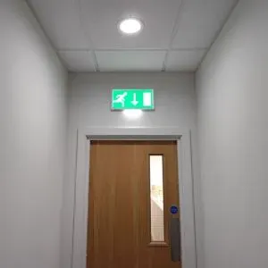 Non-maintained emergency lighting installed above a door at the end of a hallway