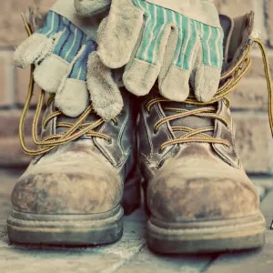 A pair of dirty steel toe cap boots with gloves on top