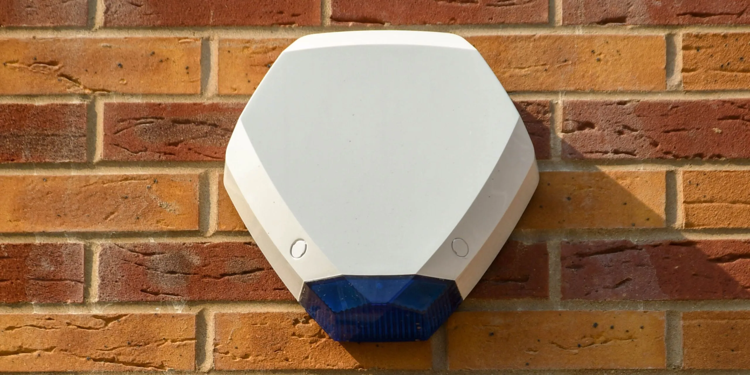 white external burglar alarm siren mounted on brick wall for home security