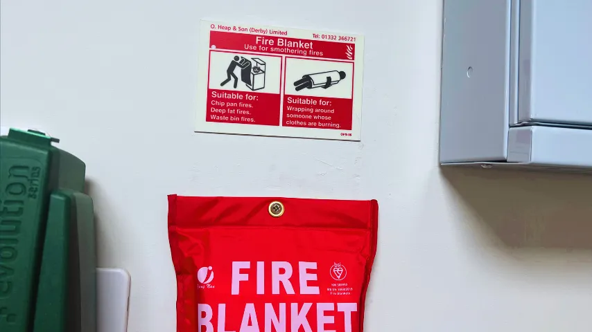 A kitchen fire blanket fitted to a wall below a fire safety sign