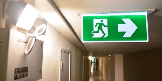 Illuminated emergency exit sign with a right arrow in a building corridor.
