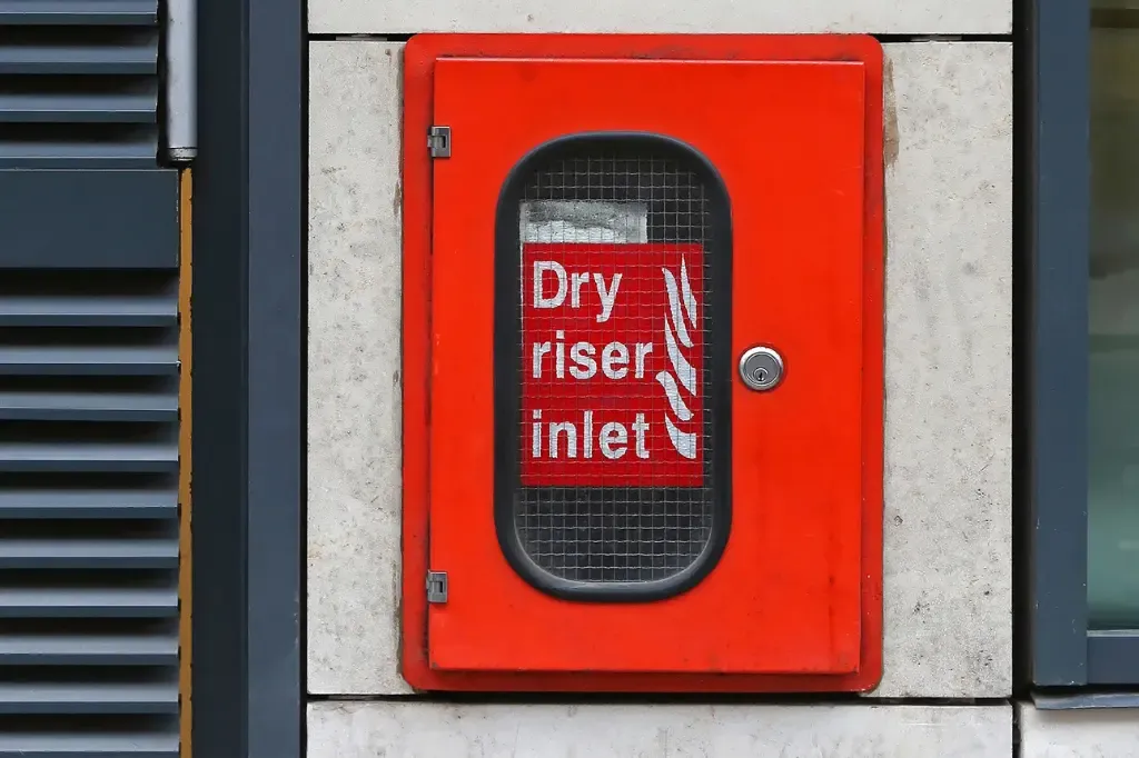 red door on a wall with a dry riser inlet sign in the window