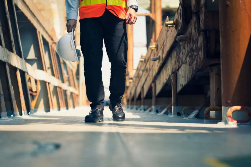 A site worker walking in a high-vis jacket and work boots with his hard hat in his hand